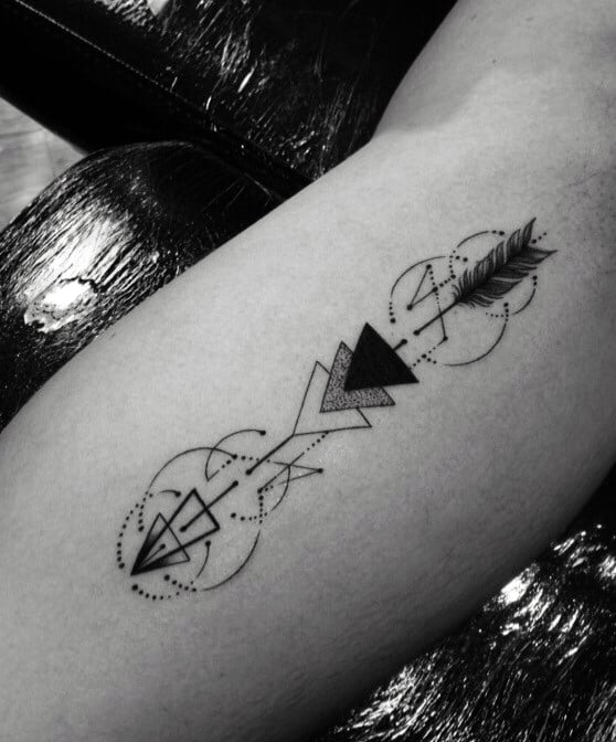 Geometric arrow tattoo featuring bold black triangles, abstract dotted circles, and sharp lines for a modern forearm design.