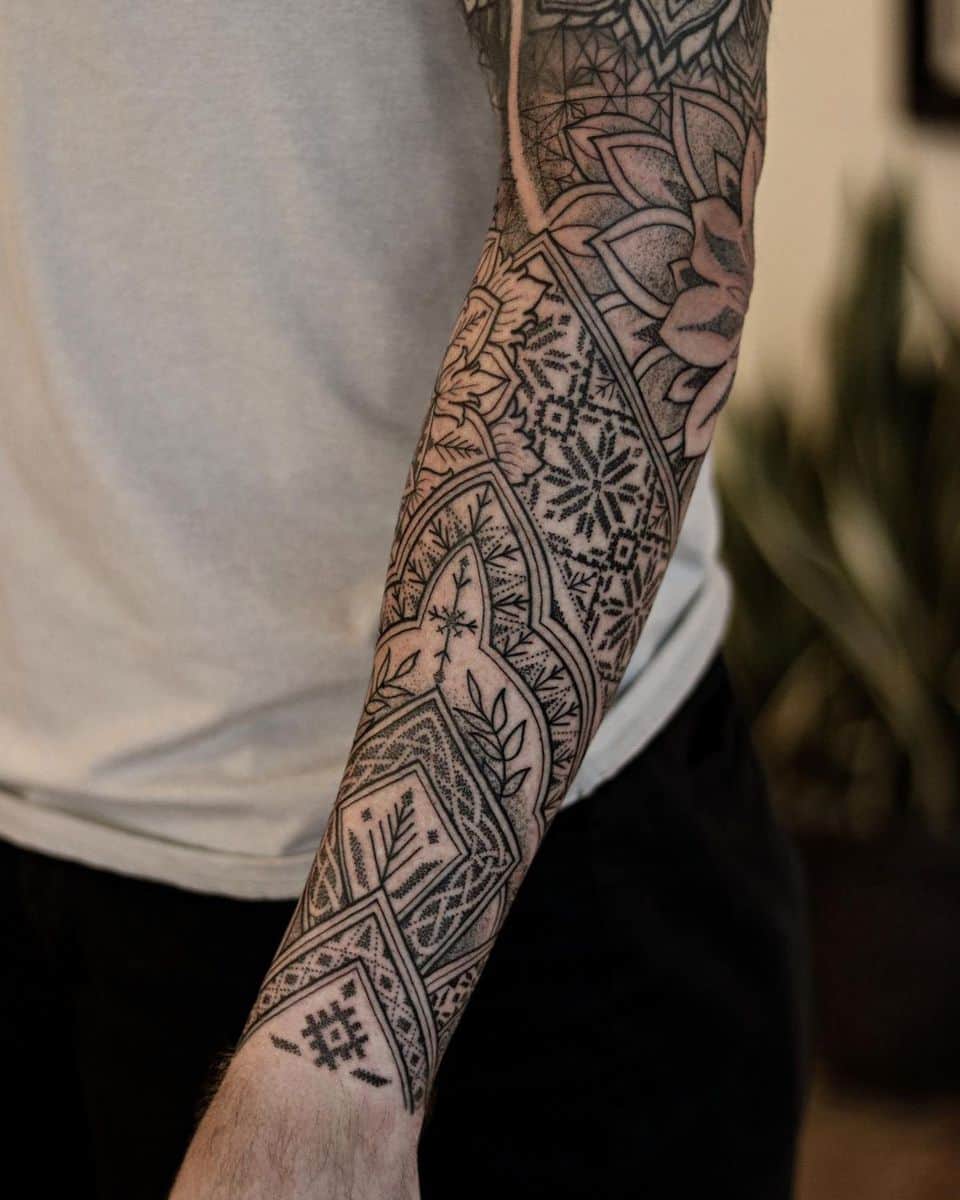 Intricate geometric blackwork tattoo covering the forearm, featuring detailed patterns, floral designs, and fine dot work
