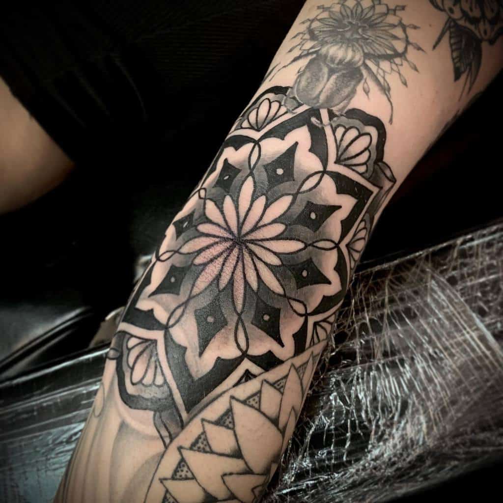 Intricate mandala tattoo with black and white geometric patterns on an arm