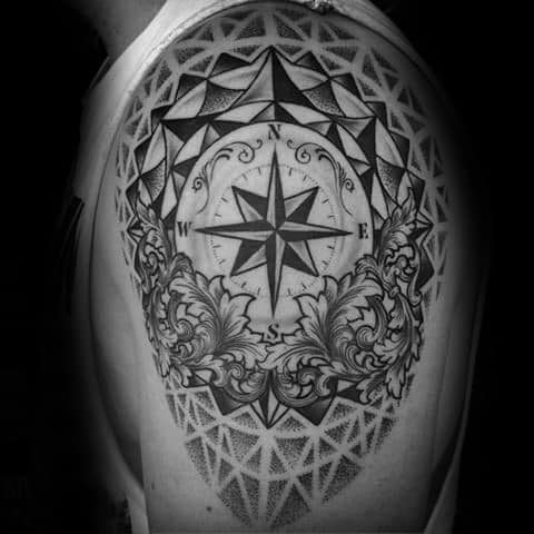 Ornate compass tattoo on shoulder with bold shading, geometric patterns, and decorative floral elements for a dramatic, detailed look.