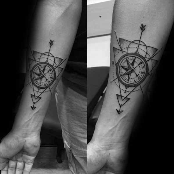 Forearm compass tattoo with bold arrows, layered triangles, and fine dotwork for a modern, geometric navigation design.
