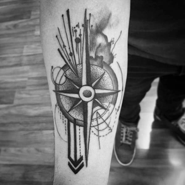 Bold compass tattoo on forearm with shaded center, abstract lines, and ink splatter effect for a dynamic, artistic look.