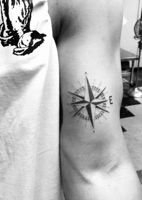 Small compass tattoo on the back of the arm with fine lines and minimalist detail, pointing east for subtle directional symbolism.