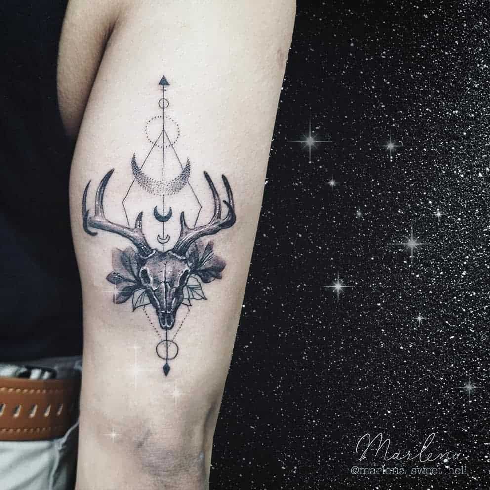 Geometric deer skull tattoo with celestial elements, including crescent moons and arrows, blending mysticism and nature in a detailed design
