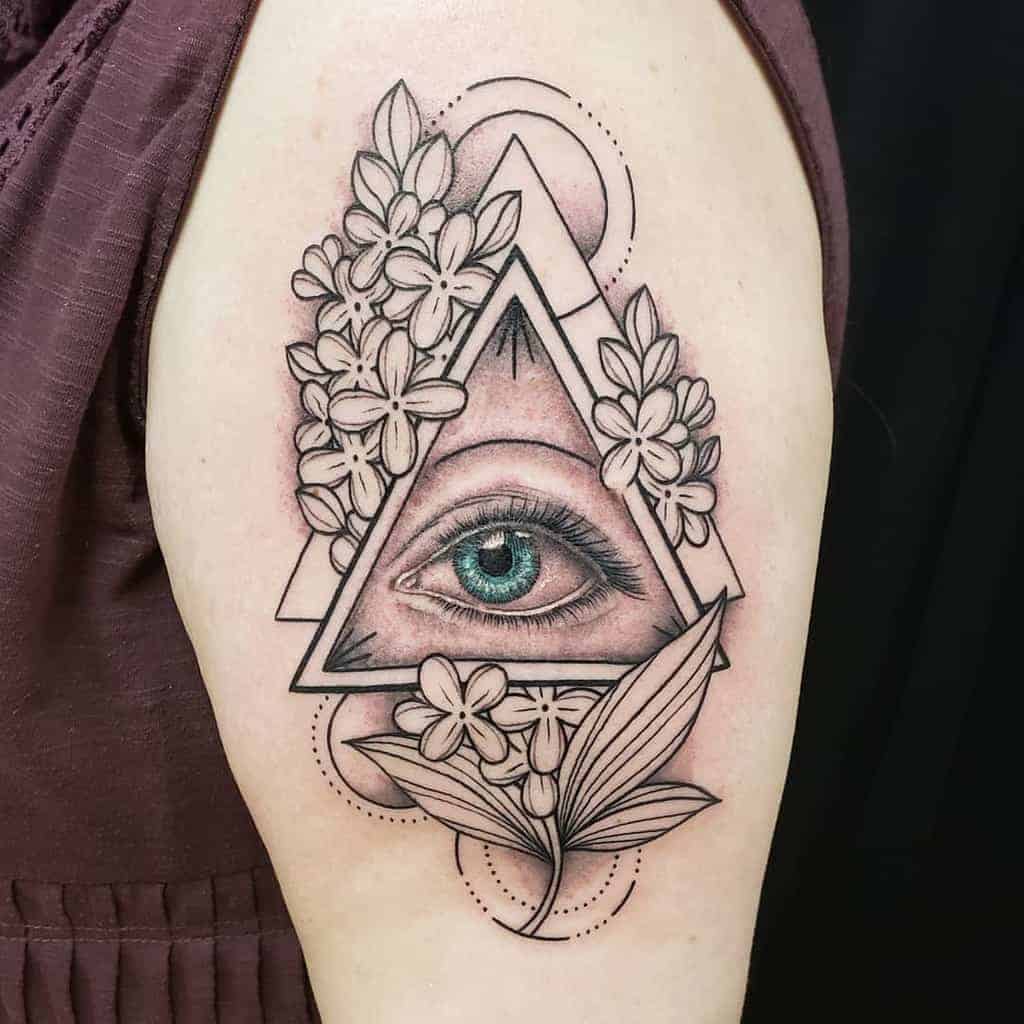 Geometric tattoo featuring a realistic blue eye within a triangle, surrounded by lilac flowers and leaves, blending intricate line work and shading