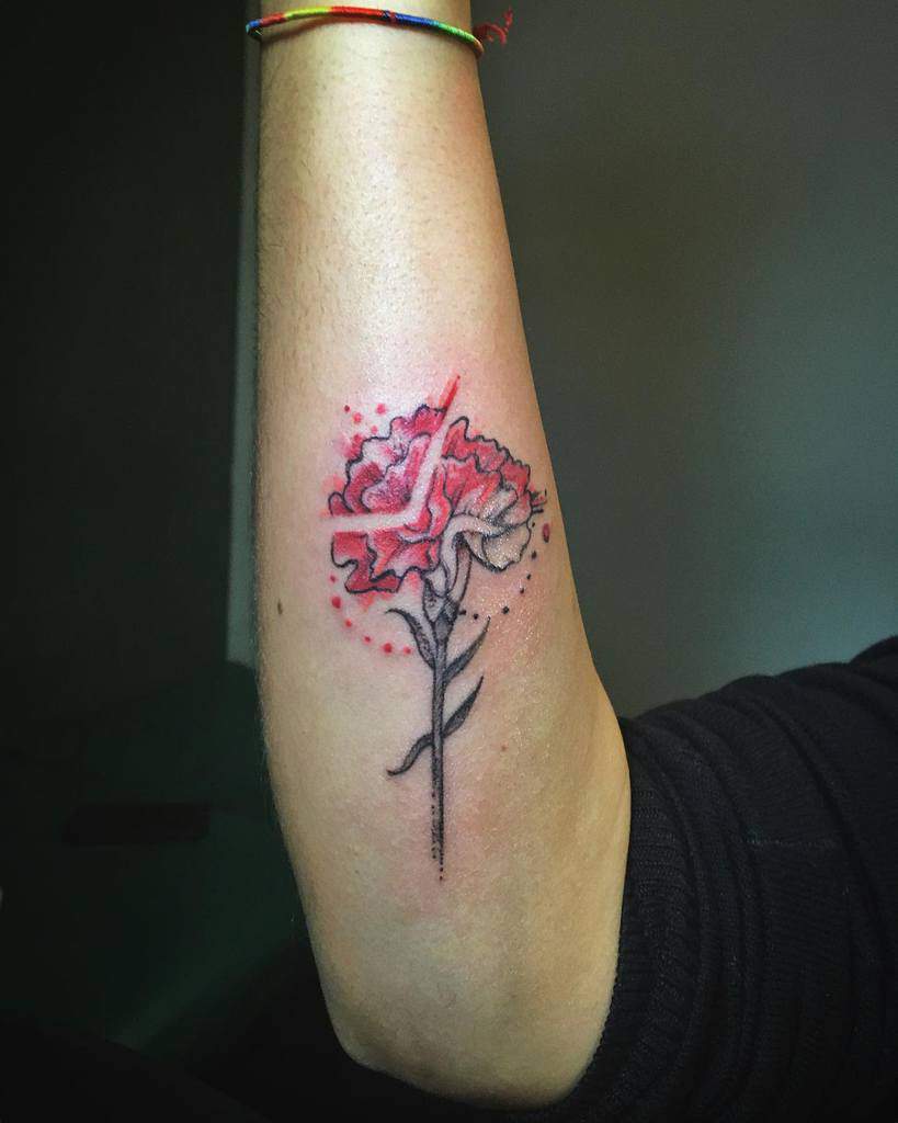 Tattoo of a red carnation with dotted accents and shading, showing a side profile of a long stem and leaves