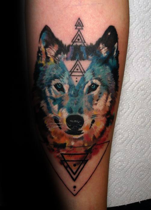 Watercolor wolf tattoo with intense blue eyes, framed by geometric triangle patterns for a bold, mystical, and modern design.
