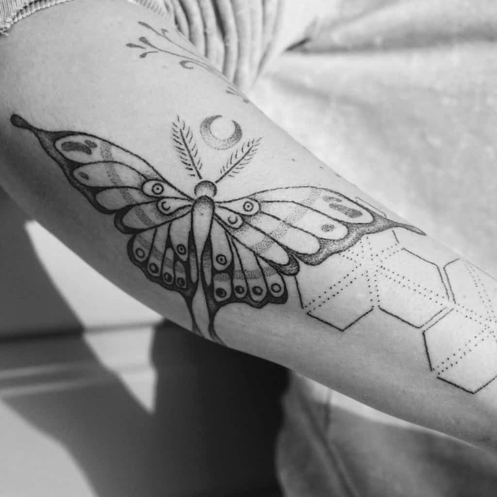 A black and grey Luna Moth tattoo with hexagonal patterns beneath, a crescent moon, and delicate lines