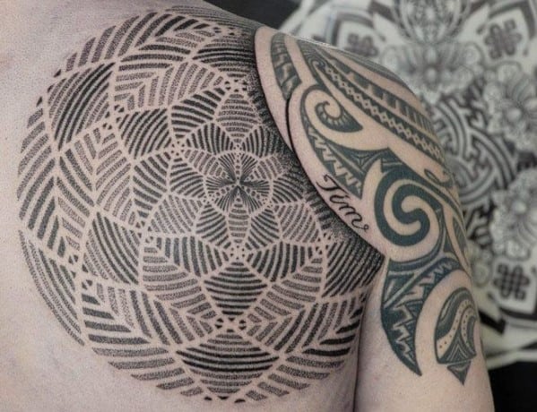 Intricate geometric and Polynesian-inspired tattoos on a person's shoulder and arm