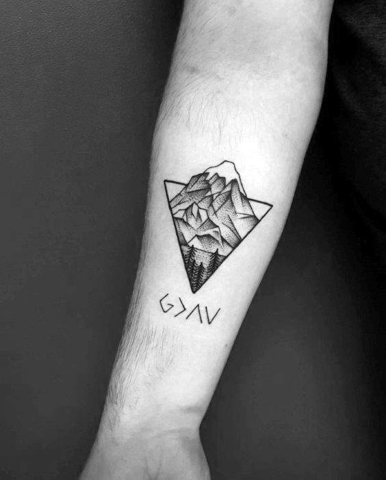 Triangle tattoo of a mountain landscape with trees, paired with stylized text or symbols beneath on the inner forearm.