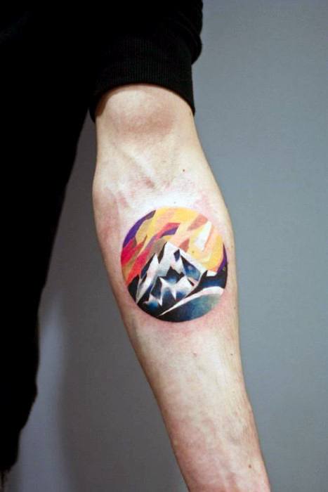 Colorful circular tattoo of stylized mountains with a vibrant abstract sunset sky in shades of orange, pink, and purple.