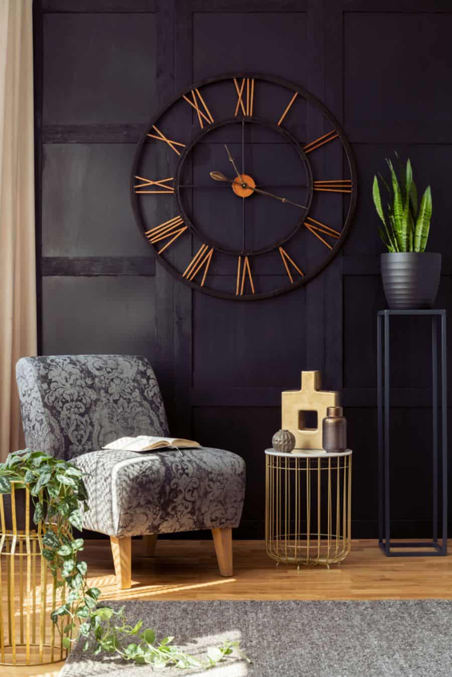 Cozy room with a patterned armchair, large clock, and plants against a dark textured accent wall