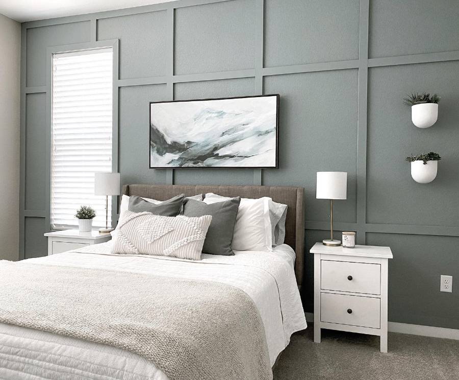 Modern bedroom with green accent wall, white bed linens, two nightstands, lamps, artwork, and small plants