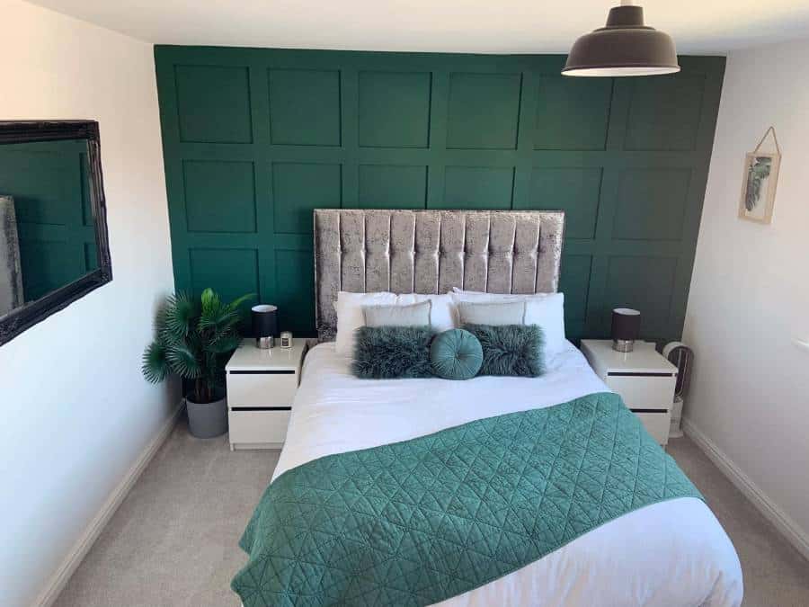Bedroom with lush accent wall, plush headboard, green bed runner, decorative pillows, and modern decor with plants