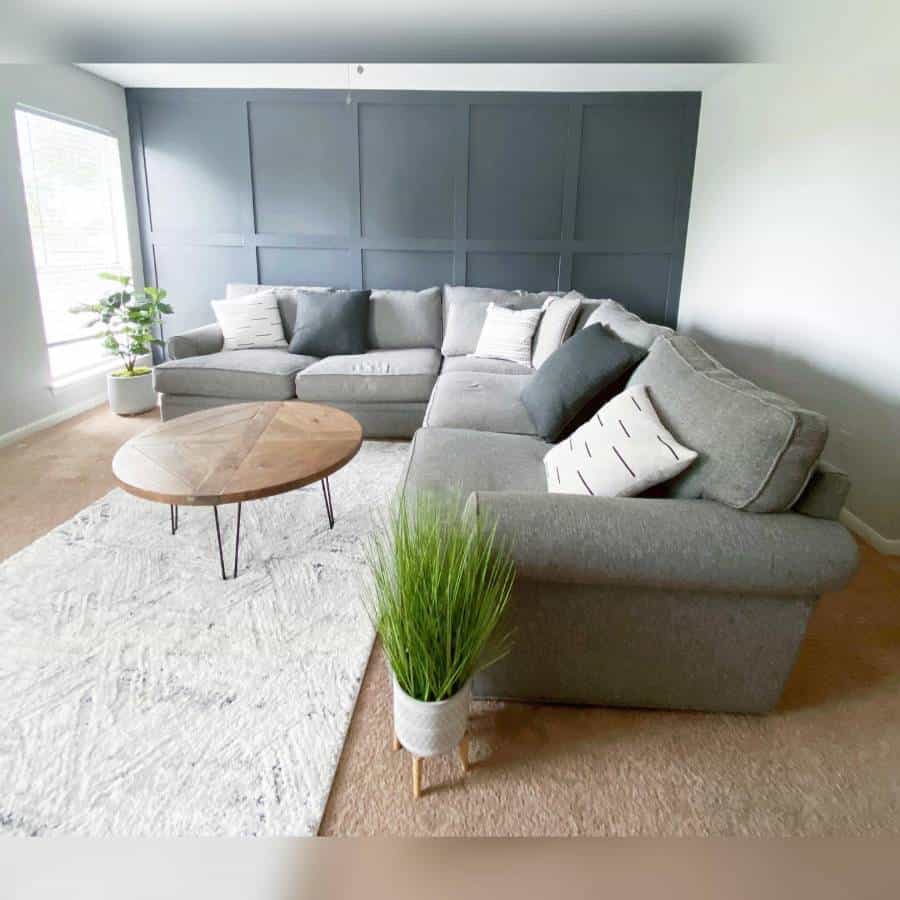 Living room with gray sectional sofa, round wooden coffee table, plants, and a striking dark accent wall