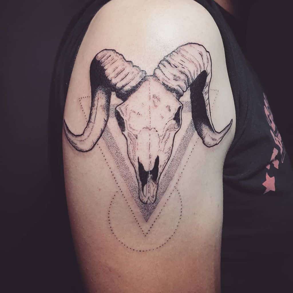 Tattoo of a ram skull with large curved horns, centered within a geometric design on an upper arm