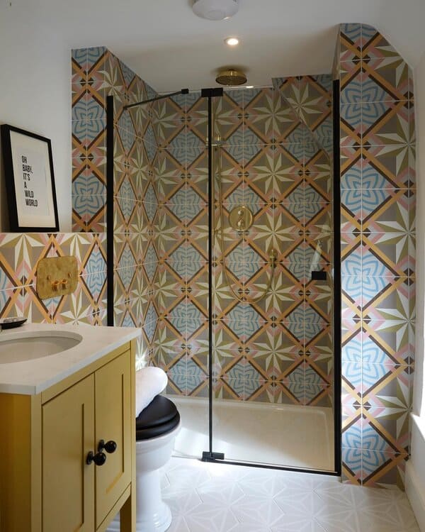 Bathroom with pastel geometric tiles in the shower and a mustard vanity featuring black hardware for a bold, playful look.