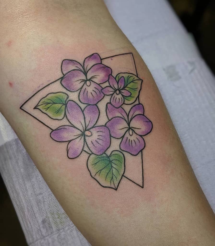 Vibrant violet flower tattoo with green leaves inside a geometric triangle outline, blending nature and modern design in a delicate composition