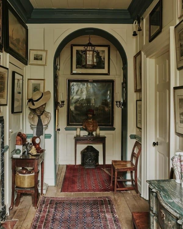 Hallway with white paneling, green trim, antique furniture, and a gallery of artwork, accented by rich, patterned rugs on wooden floors.