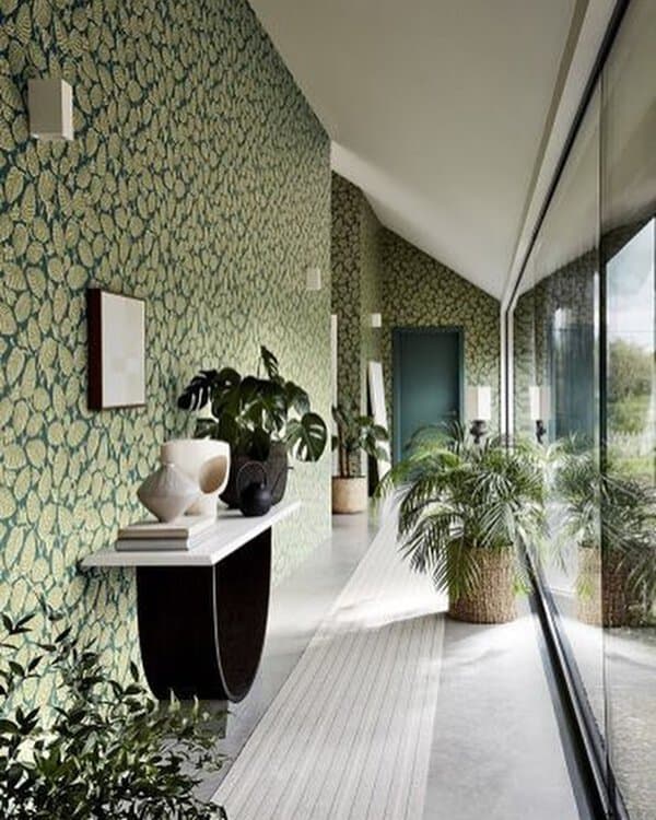 Green botanical wallpaper adds texture and depth to the hallway, complemented by sleek furniture and plants.