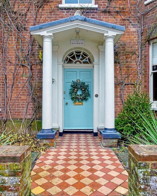 Turquoise Georgian door with white columns, fanlight detail, and a checkered tile path in front of a red-brick facade.