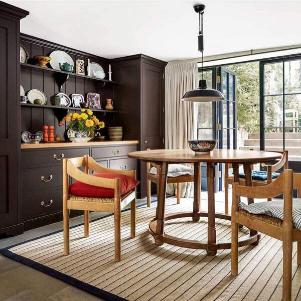Dark cabinetry, a round wooden table, and open shelves with decorative ceramics create a bold yet warm area for meals.