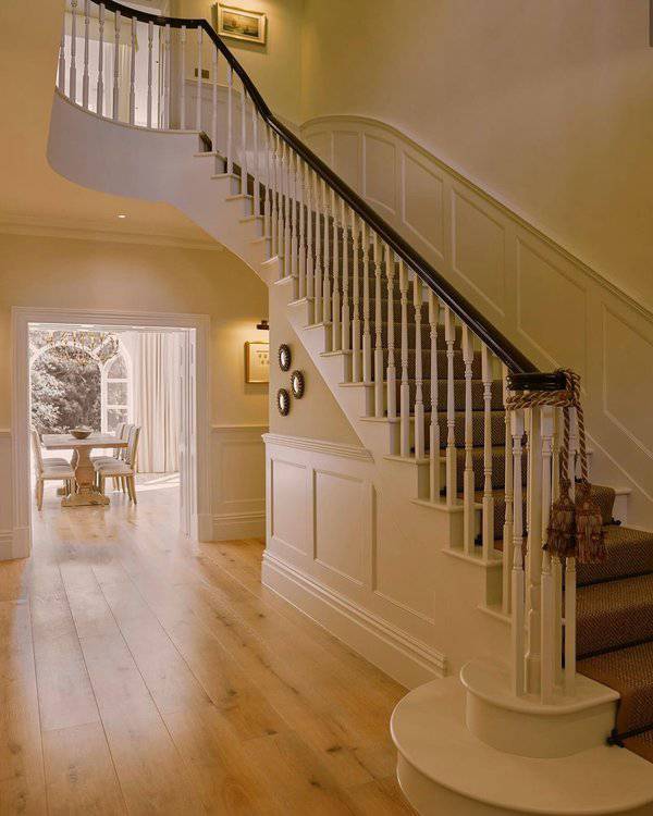 Curved white staircase with warm wood floors, crisp paneling, and a bright hallway leading to a classic dining space.