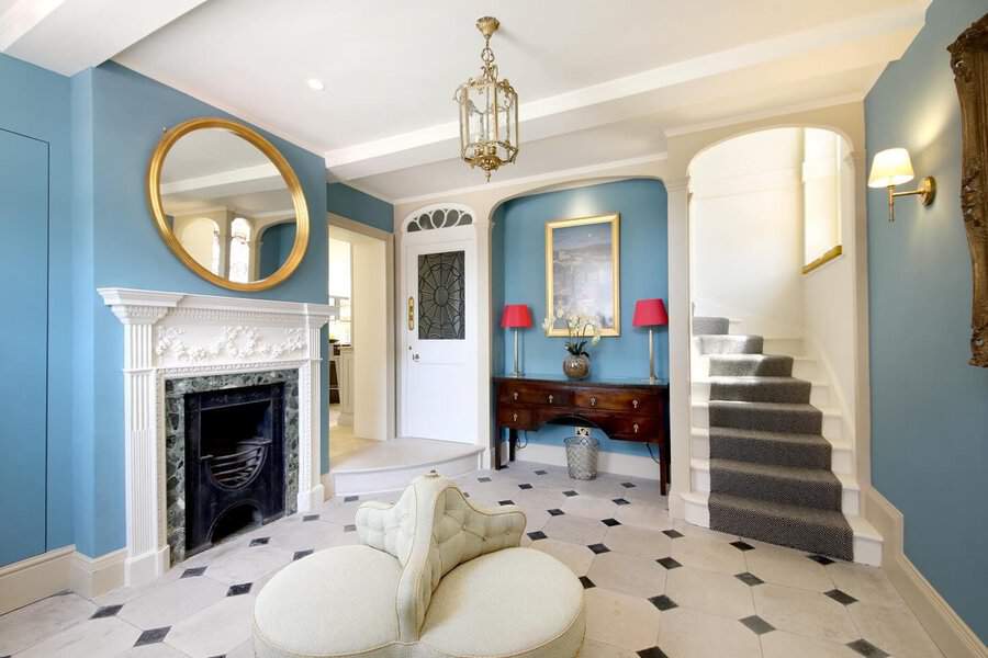Elegant entryway with blue walls, a gold mirror, marble-patterned flooring, and classic furniture. A warm, welcoming space for any home.