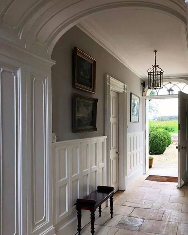 Georgian entry hall with tall white paneling, arched ceiling, gray walls, and a simple bench leading to a bright garden view.