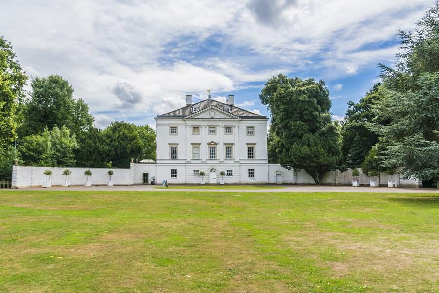 Grand white British Georgian house with a pediment and symmetrical windows, set behind a sweeping green lawn.