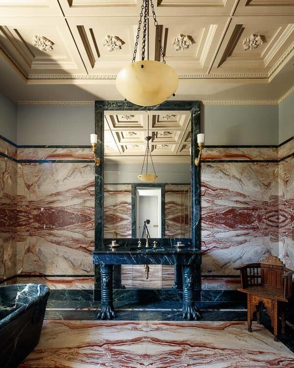 Opulent bathroom with multi-toned marble walls, a black marble tub, ornate ceiling moldings, and an arched window for a palatial feel.