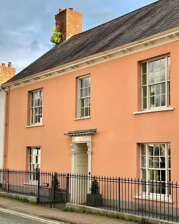 Peach Georgian house with symmetrical sash windows, a refined doorway, and a tall brick chimney behind a wrought-iron fence.