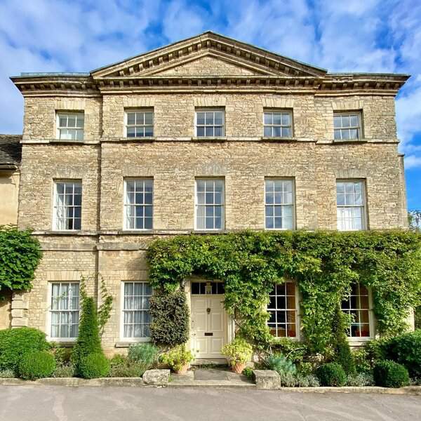 Stone Georgian house with symmetrical windows, a white front door, and trailing green vines for a romantic, timeless look.