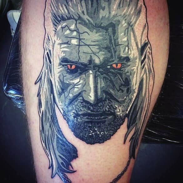 Geralt tattoo in a bold black and gray style, featuring glowing red eyes, deep scars, and a rugged, battle-worn expression.