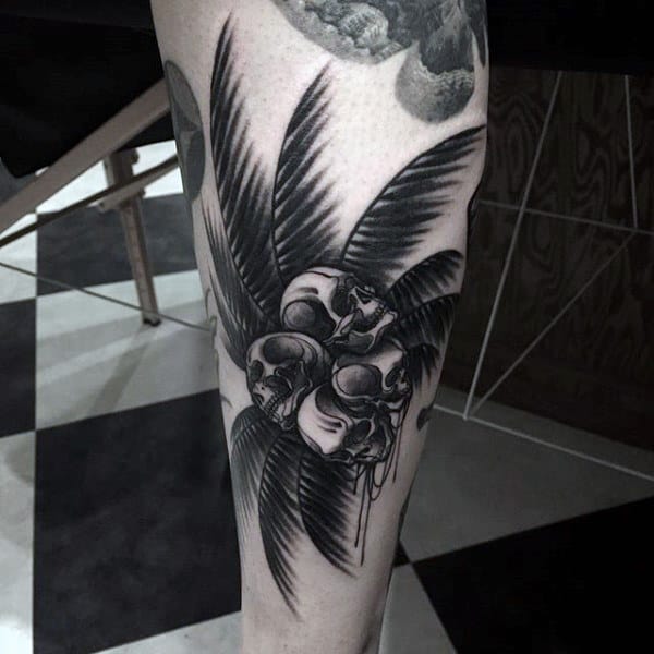 Tattoo of three skulls intertwined with palm leaves on a leg