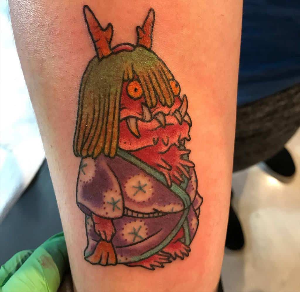 Vibrant tattoo of the radish spirit from Spirited Away, featuring a red, horned creature in a patterned kimono with exaggerated details