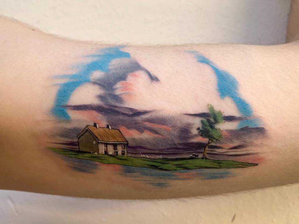 Scenic Spirited Away tattoo of Zeniba’s cottage on a peaceful island, with a watercolor-style sky, clouds, and serene reflections