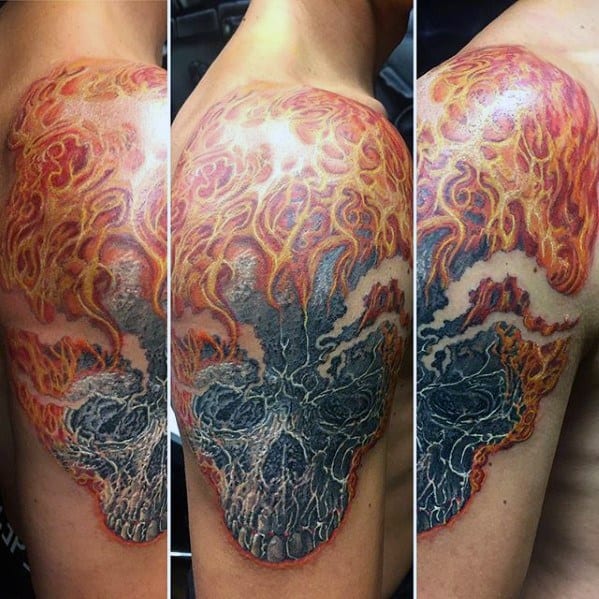 Ghost Rider shoulder tattoo with a textured skull and vivid flames rising upward in fiery orange, red, and yellow tones.