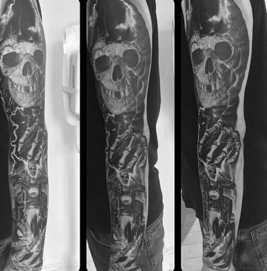 Black and grey Ghost Rider full sleeve tattoo with a large skull, chains, and dark motorcycle elements surrounded by stormy shading.