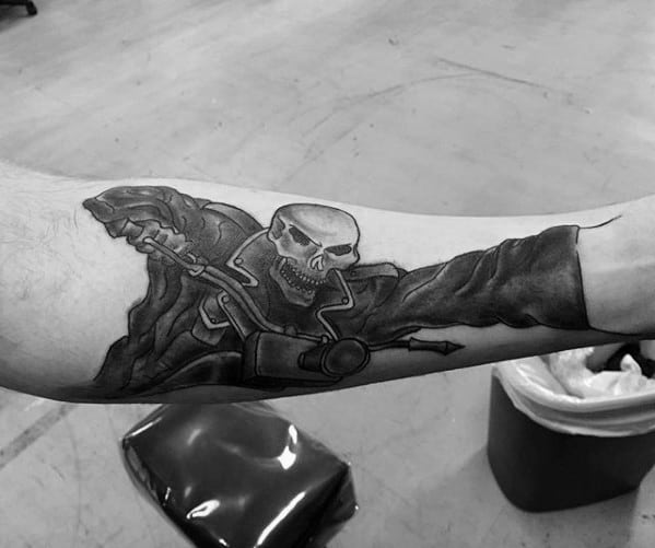 Black and grey Ghost Rider forearm tattoo showing the character gripping motorcycle handlebars with a fierce skull and flowing jacket.