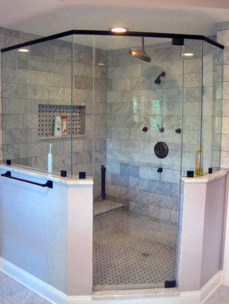 Corner glass-enclosed shower with marble tiles, a bench, built-in shelving, silver fixtures, and black trim