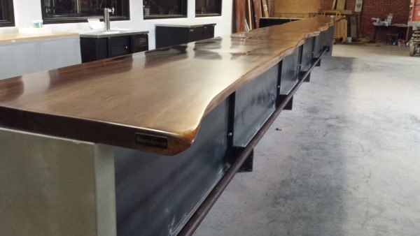 Polished live edge wood slab bar top with sleek black base in a modern industrial setting.