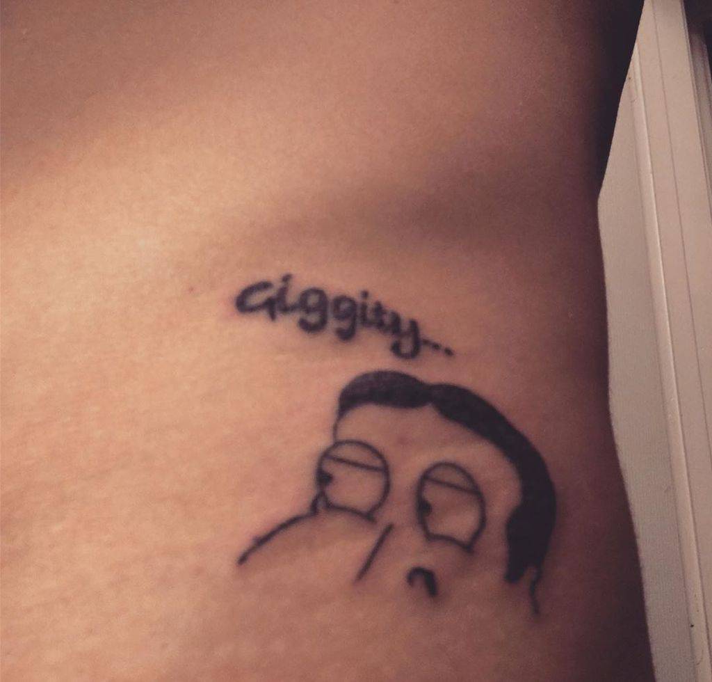 A black ink tattoo of a cartoon character's face with the phrase 'Giggity...' above, placed on the ribs in a humorous and minimalist style.