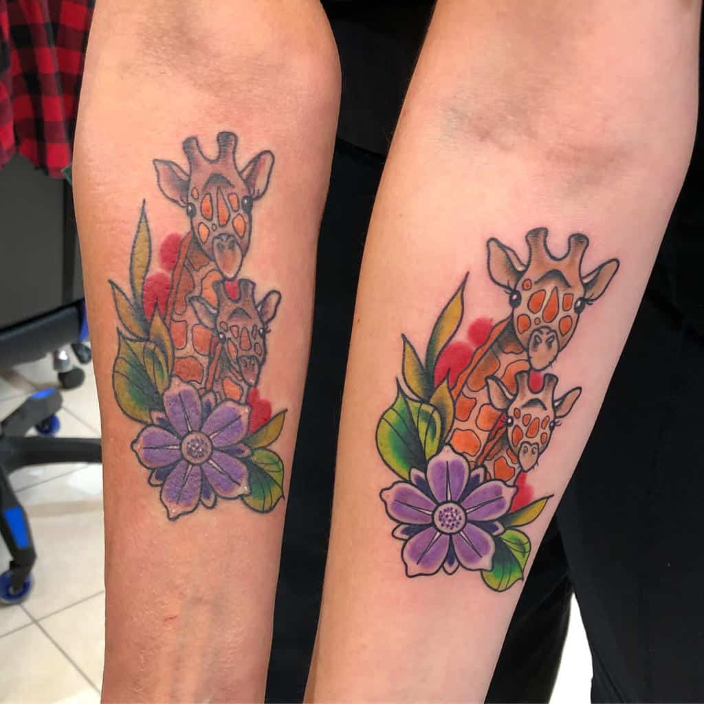 Matching mother-daughter tattoos of two giraffes surrounded by vibrant flowers and leaves