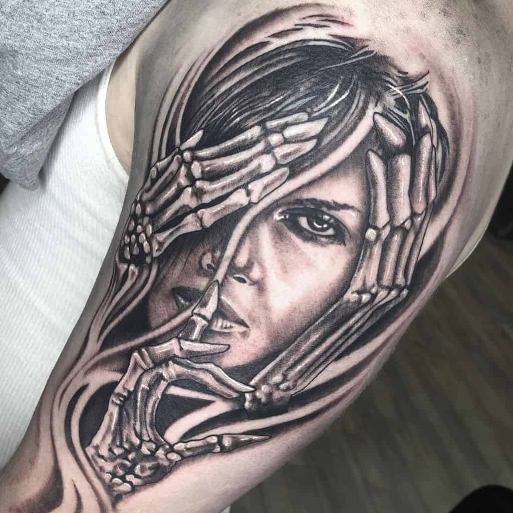 Tattoo of a woman's face partially covered by skeletal hands on an upper arm