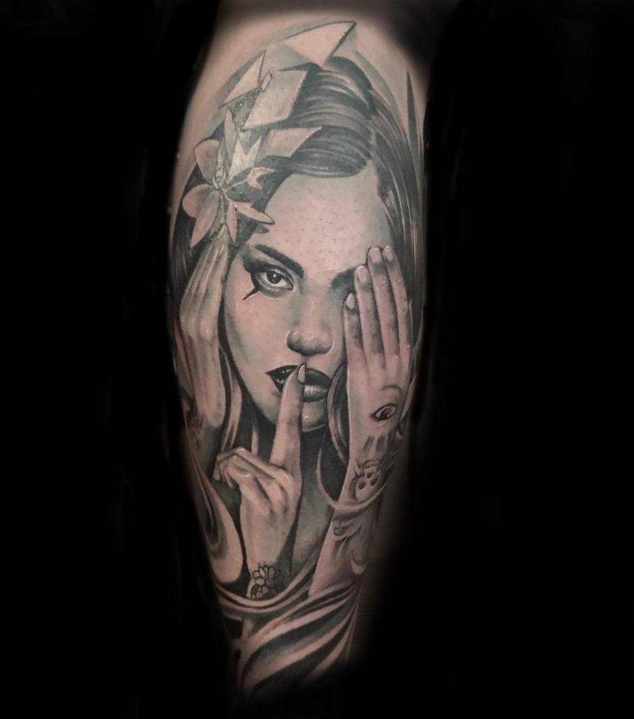 Tattoo of a woman with finger on lips, covering one eye, and wearing a geometric headpiece