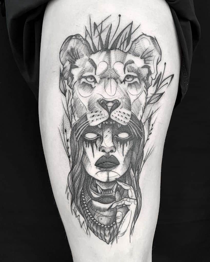 Black and grey tattoo on the thigh featuring a fierce lioness headdress over a mystical woman with white eyes and tribal markings.