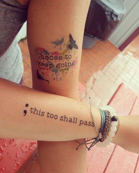 The image shows two tattoos on the arms. The tattoo on the upper arm reads "Choose to keep going" with a watercolor-like effect and birds flying. The tattoo on the lower arm features a semicolon followed by the phrase "this too shall pass" in delicate script.