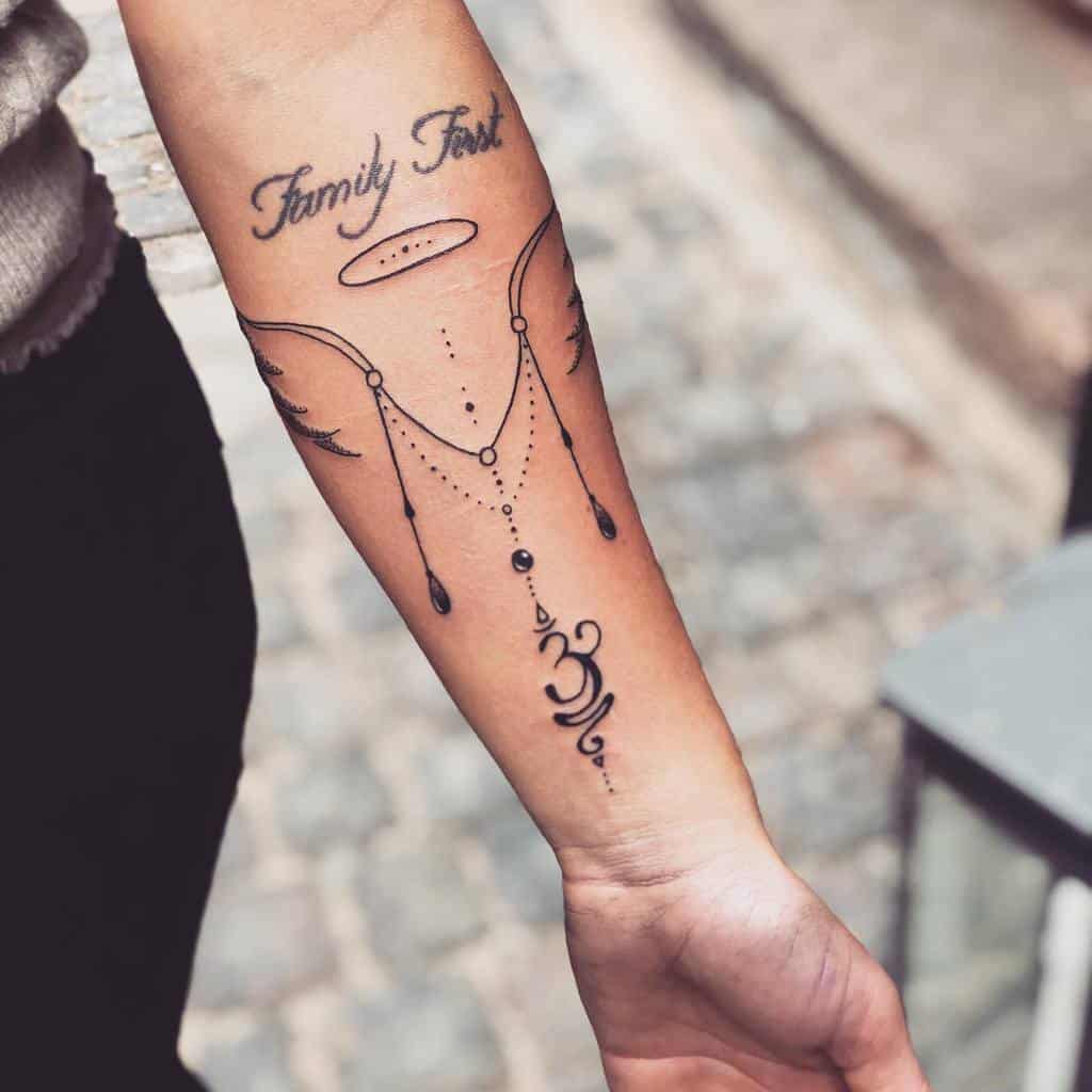 Elegant tattoo with minimalist angel wings, a halo, delicate chains, and "Family First" script