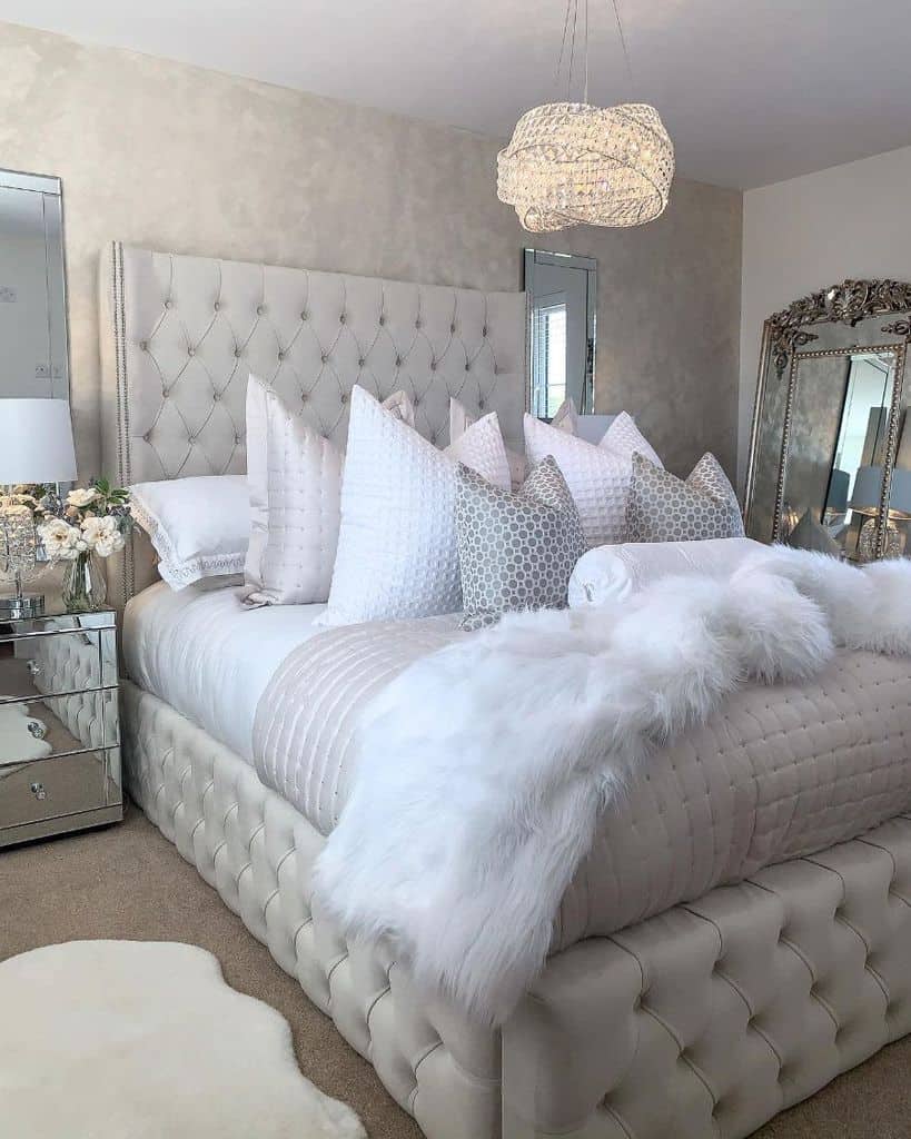 Luxurious tufted bed with layered pillows, faux fur throw, and mirrored bedside table.